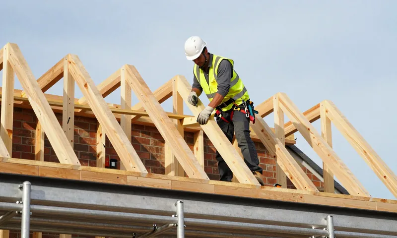 A carpenter fixing the bracing of triangular roof trusses from a scaffold