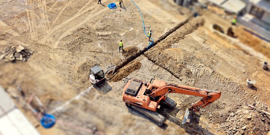 Level 2 Diploma in Ground Works Operations2 Manual workers and Engineers are digging a raw in the ground, they do drainage, sewer system, then make a new asphalt road. Directly above, tilt-shift.