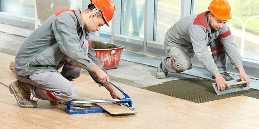 Two industrial tiler builder worker installing floor tile at repair renovation work