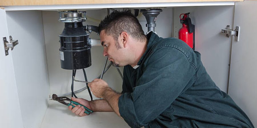 A plumber laying under a house hold sink working on a garbage disposal. A plumber laying under a house hold sink working on a garbage disposal.